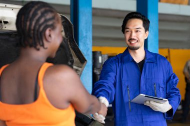 Garaj servisindeki üniformalı Afrikalı kadının portresi. Müşteriyle tokalaşıyor ve bir arabayı kontrol ederken dijital tablet tutuyor.