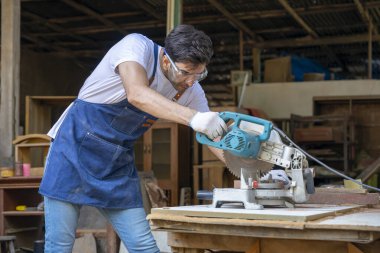 Genç, beyaz bir erkek dairesel testereyle odun kesiyor, zanaatkar evde ahşap döşeme ve onarım yapıyor, insan hobileri kavramı, marangozluk işi, tamirat, DIY 
