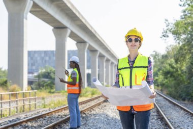 Portre mühendisi demiryolu inşaat müfettişi elinde proje tasarısı, demiryolu raylarında çalışıyor, geçmişi bulanık Afrikalı teknisyen meslektaşı 