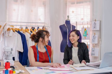 Mor saçlı genç, havalı Asyalı kadın tasarımcı terzi, yaratıcı yeni moda koleksiyonuyla kıyafet modelini tartışıyor.