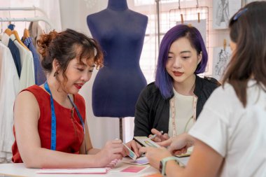 Terzi ve moda tasarımcısı iş ortaklığı renk örnekleri ve çizimler ile kıyafet tasarımını bir müşteriye açıklıyor, atölyede çalışan kadın moda tasarımcısı