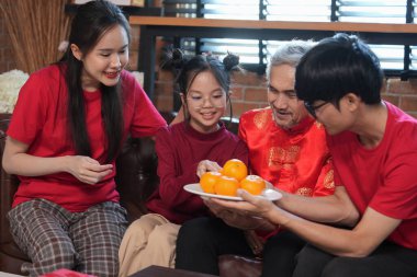 Mutlu Asyalı aile, Çin Yeni Yılı 'nı kutlamak için evde toplanıyor, kanepede oturuyor, konuşuyor, kırmızı zarf veriyor ve yemek yiyor.
