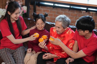 Mutlu Asyalı aile, Çin Yeni Yılı 'nı kutlamak için evde toplanıyor, kanepede oturuyor, konuşuyor, kırmızı zarf veriyor ve yemek yiyor.