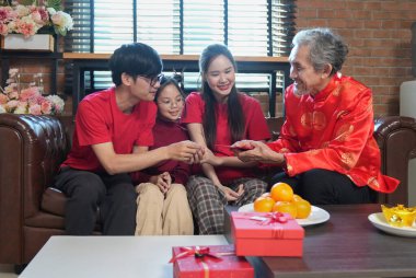 Mutlu Asyalı aile, Çin Yeni Yılı 'nı kutlamak için evde toplanıyor, kanepede oturuyor, konuşuyor, kırmızı zarf veriyor ve yemek yiyor.