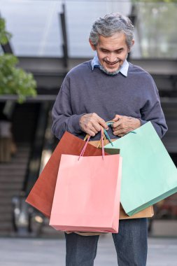 Alışveriş çantaları taşıyan mutlu Asyalı son sınıf öğrencisi, alışveriş merkezinin önünde dikiliyor.