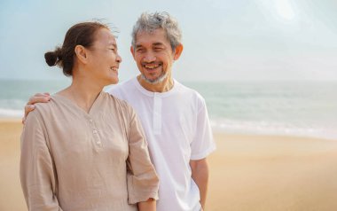 Romantik Asyalı son sınıf çifti kumsalda yürüyor, gülümsüyor, birbirlerine bakıyor, mutlu mesut konuşuyorlar, yaşlılar yaşam tarzı, aile, seyahat, varış yeri kavramı                                