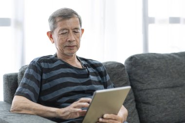 Teknolojiyle yaşlı modern yaşam tarzı kavramı, oturma odasında dijital tablet kullanan kıdemli adam.