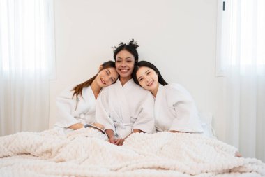 Bornozlu genç, çok ırklı arkadaşların portresi. Yatakta oturup, birlikte kutluyor, eğleniyor, gülüyor ve spa odasında dinleniyorlar.