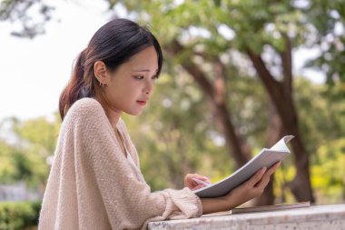 Genç çekici Asyalı kız masada oturuyor, tek başına kitap okumaya odaklanıyor, kampüste öğrenim görüyor, bilgiye çalışıyor.