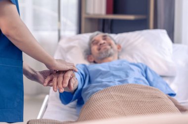 Üniformalı bir hemşireye bakan, onu destekleyen, el ele tutuşan ve cesaretlendiren yaşlı bir erkek hasta görülüyor.