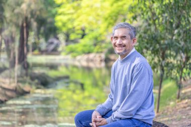 Orman parkında oturan Asyalı kıdemli adam, yaşlılar seyahat ediyor, dinleniyor.