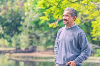 Mutlu Asyalı son sınıf öğrencisi portresi parkta duruyor, yaşlılar seyahat ediyor, rahatlıyor.
