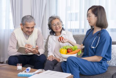 Üniformalı ev sağlık hemşiresi yaşlı çifte meyve, vitamin ve diyet liflerinin besin değerini açıklıyor.