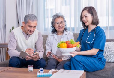 Üniformalı ev sağlık hemşiresi yaşlı çifte meyve, vitamin ve diyet liflerinin besin değerini açıklıyor.