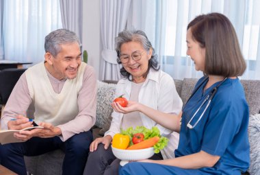 Üniformalı ev sağlık hemşiresi yaşlı çifte meyve, vitamin ve diyet liflerinin besin değerini açıklıyor.