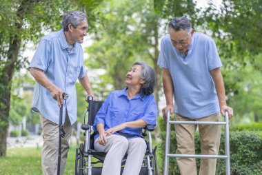 Tekerlekli sandalyesi, yürüteci ve bastonu olan üç yaşlı arkadaş doğa parkında, yaşlanan toplumda ve sağlık hizmetleri konseptinde birlikte konuşmaktan keyif alıyorlar.