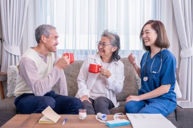 Üniformalı bir hemşire evde müşteri ziyaretinde sağlıklı içecek, süt, meyve suyu ya da vitamin gibi konuları anlatırken aynı zamanda yaşlı bir çiftle eğleniyor.