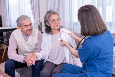 Üst düzey bir çift fiziksel muayene oluyor, üniformalı hemşire steteskop kullanıyor bir kadının göğsünü dinlerken koca karısını cesaretlendirmek için el ele tutuşuyor.