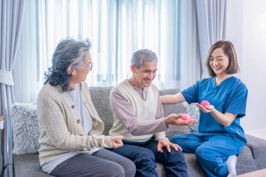 Üniformalı neşeli bir terapist yaşlı çiftleri bir topla, fizik tedaviyle ve rehabilitasyonla el ele tutuşmaları için eğitiyor.