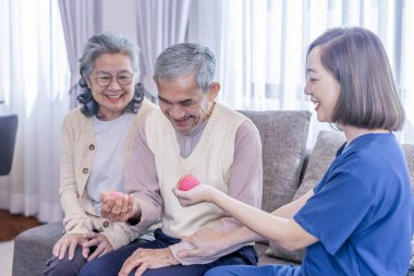 Üniformalı neşeli bir terapist yaşlı çiftleri bir topla, fizik tedaviyle ve rehabilitasyonla el ele tutuşmaları için eğitiyor.