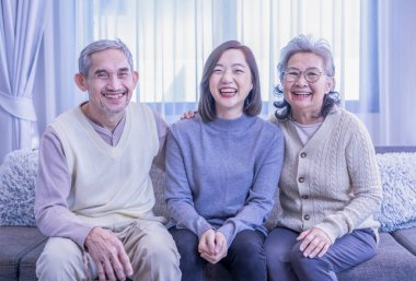 Asyalı bir ailenin portresi. Oturma odasında birlikte vakit geçirmenin keyfini çıkarın. Kanepede oturup, kucaklaşmanın, mutlu bir şekilde gülümsemenin.