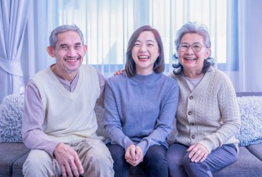 Asyalı bir ailenin portresi. Oturma odasında birlikte vakit geçirmenin keyfini çıkarın. Kanepede oturup, kucaklaşmanın, mutlu bir şekilde gülümsemenin.