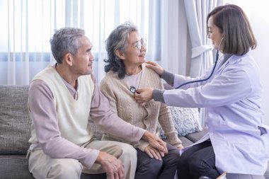 Üst düzey bir çift, üniformalı bir doktor tarafından muayene ediliyor. Steteskop kullanıyor. Yaşlı kadını dinliyor.