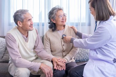 Üst düzey bir çift, üniformalı bir doktor tarafından muayene ediliyor. Steteskop kullanıyor. Yaşlı kadını dinliyor.