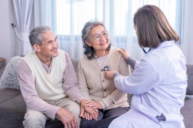 Üst düzey bir çift, üniformalı bir doktor tarafından muayene ediliyor. Steteskop kullanıyor. Yaşlı kadını dinliyor.