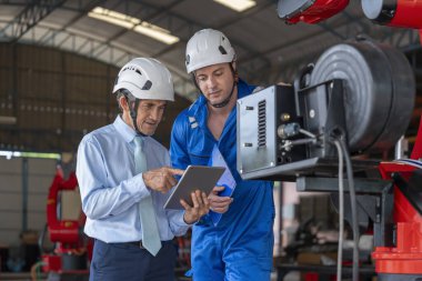 Bakım robotu makinesindeki fabrika işçileri, kıdemli uzman yönetici tablet bilgisayar kullanıyor. Küçük sektörde çalışan beyaz erkek teknisyen tavsiye veriyor.