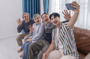 Asyalı aile ve arkadaşlarının portresi evde buluşuyor, kanepede oturuyor ve oturma odasında selfie çekiyor.