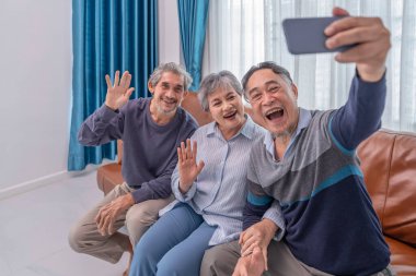 Asyalı aile ve arkadaşlarının portresi evde buluşuyor, kanepede oturuyor ve oturma odasında selfie çekiyor.