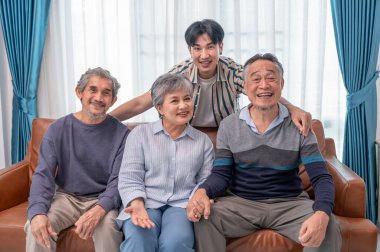 Asyalı aile ve arkadaşlarının portresi evde buluşuyor, oturma odasında kanepede oturuyor, kameraya poz veriyor.