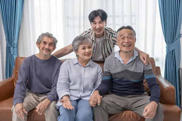 Asyalı aile ve arkadaşlarının portresi evde buluşuyor, oturma odasında kanepede oturuyor, kameraya poz veriyor.