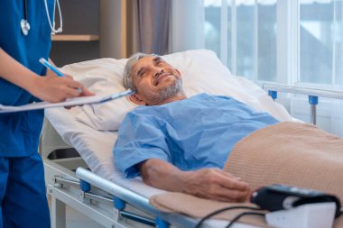 Yatakta yatan kıdemli bir hastanın hasta semptomlarını izlemek için elinde tıbbi rapor olan bir hemşireyle konuştuğu olay yeri.