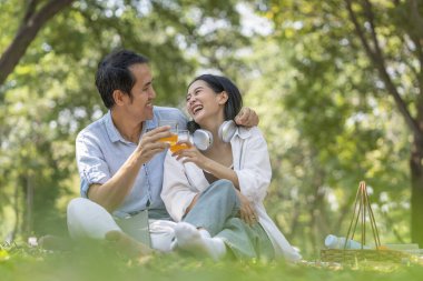 Romantik genç Asyalı çift boş zamanlarını parkta dinlenerek, piknik yaparak, oturarak, gülümseyerek ve meyve suyu içerek geçirirler.