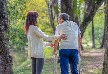 Genç Asyalı kadın bakıcı Doğa Parkında Walker 'la yürüyen yaşlı adama yardım ediyor, yaşlı rehabilitasyon, sağlık hizmetleri