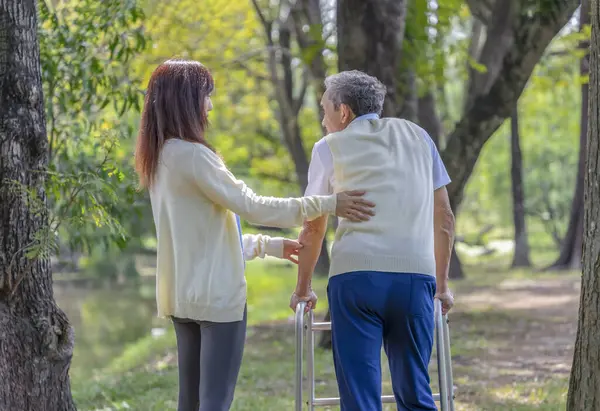 Genç Asyalı kadın bakıcı Doğa Parkında Walker 'la yürüyen yaşlı adama yardım ediyor, yaşlı rehabilitasyon, sağlık hizmetleri