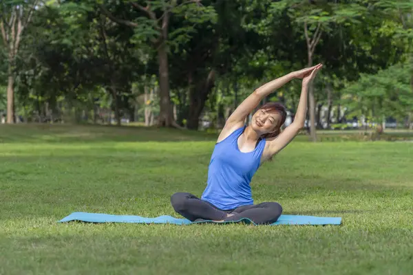 Genç Asyalı kadın minder üzerinde yoga yapıyor, parkta meditasyon yapıyor, güç ve esneklik.