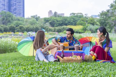 Bir grup renkli lgbtq gökkuşağı kıyafetli arkadaş parkta piknik yapıyorlar, konuşuyorlar, gitar çalıyorlar, şarkı söylüyorlar, konsept lgbtq mutlu gurur ayı