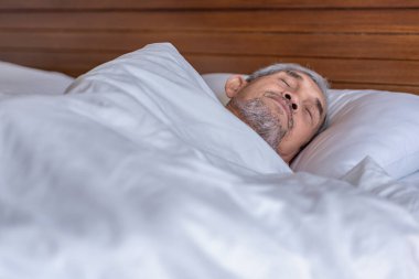 Son sınıf öğrencisi, beyaz bir battaniyenin altında rahat bir şekilde yatıyor, dinleniyor, sıcak bir odada uyuyor.