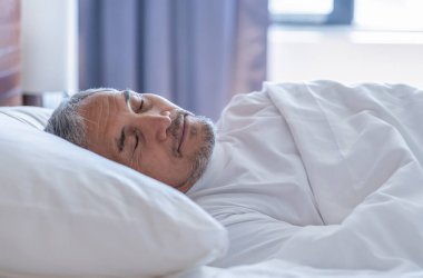 Son sınıf öğrencisi, beyaz bir battaniyenin altında rahat bir şekilde yatıyor, dinleniyor, sıcak bir odada uyuyor.