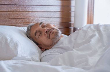 Son sınıf öğrencisi, beyaz bir battaniyenin altında rahat bir şekilde yatıyor, dinleniyor, sıcak bir odada uyuyor.