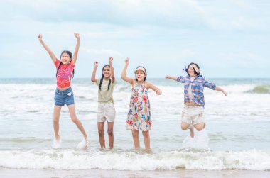 Bir grup çok ırklı çocuk, deniz kıyısında birlikte eğleniyorlar, kumsalda atlıyorlar, yaz tatillerinde seyahat ediyorlar.