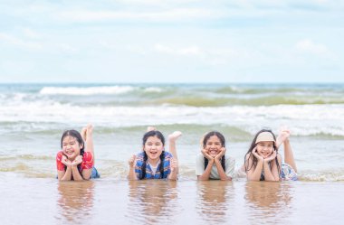 Bir grup çok ırklı çocuk ellerinde çeneleriyle kumsalda sıralanmış kameraya gülümsüyor ve poz veriyorlar.
