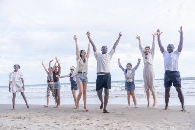 Bir grup farklı arkadaş ve aile kumsalda toplanıp akşam güneşinde el ele tutuşuyorlar.