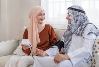 Genç Arap Müslüman evli çift oturma odasında oturuyor, kan basıncını ölçüyor, kan basıncını ölçüyor, ev tansiyonunu ölçüyor, kendi sağlığını gözetiyor.