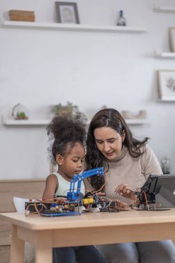 Kafkas kadın öğretmen dijital tablet kullanarak Afrikalı ilkokul öğrencisine masada robot devresi, STEM öğrenimi, eğitim kavramı üzerinde yardım ediyor.