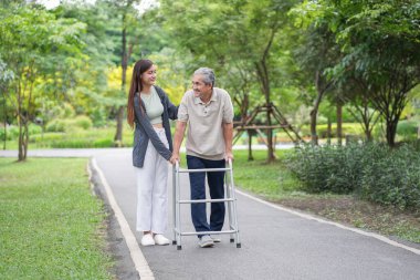 Yaşlı bir adam, genç yetişkin bir kızla parkta Walker Yardım Rehabilitasyonu 'nu kullanıyor.
