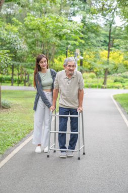 Yaşlı bir adam, genç yetişkin bir kızla parkta Walker Yardım Rehabilitasyonu 'nu kullanıyor.